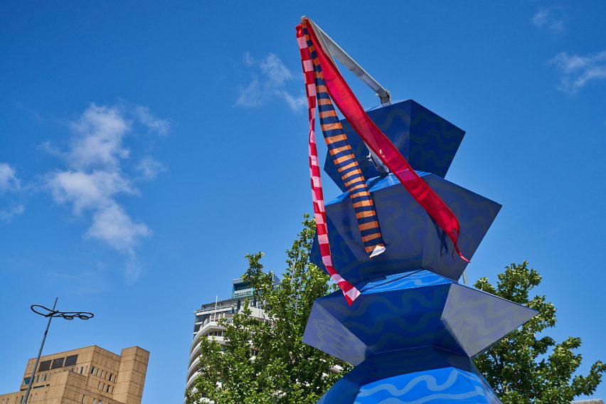 Three thin flags attached to the mast-like top of the blue Merseyside Totemy sculpture