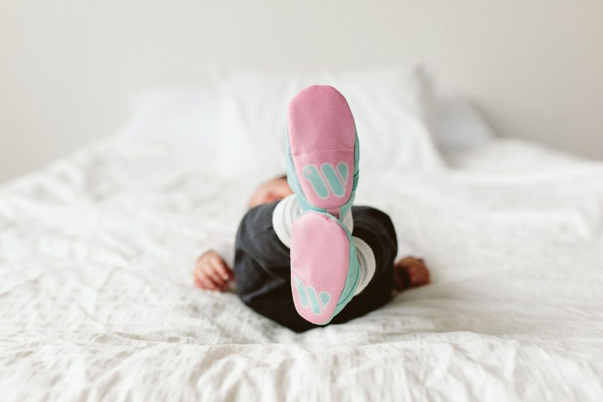 A baby lying on a bed wearing Woolybubs shoes
