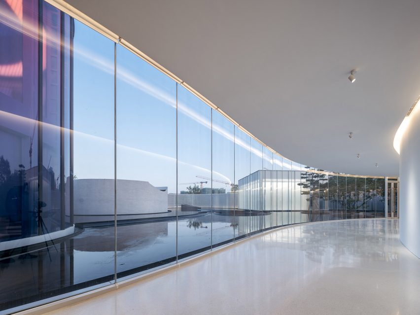 Corridor with strip lights and glass walls with views to water feature and curved buildings
