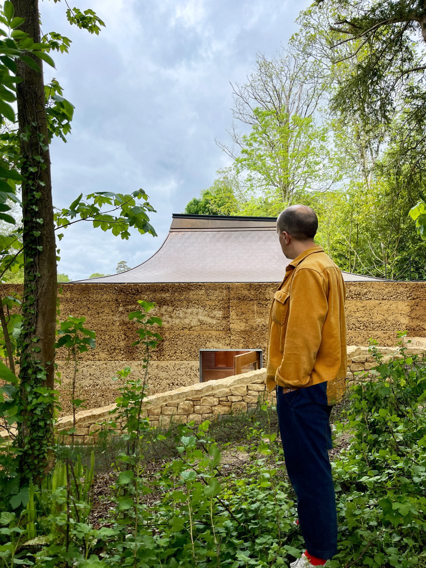 Человек, стоящий рядом с домом из утрамбованной земли от Invisible Studio