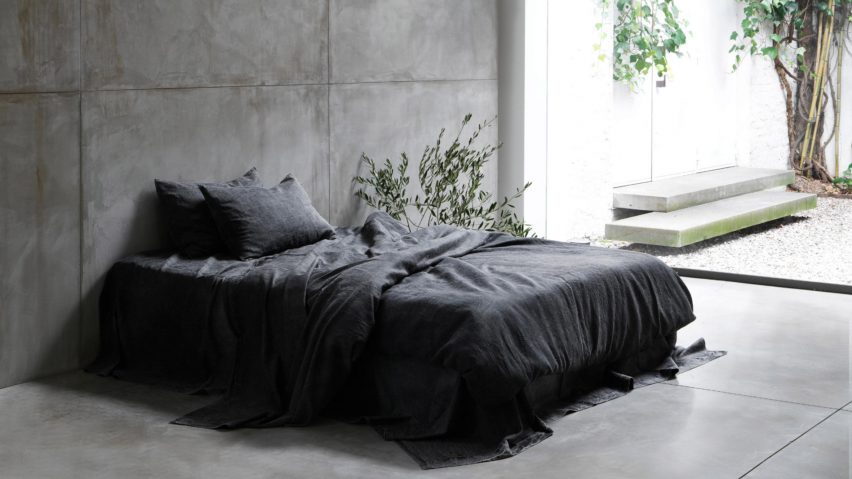 Photograph showing bed in concrete-walled bedroom with charcoal-coloured bedding