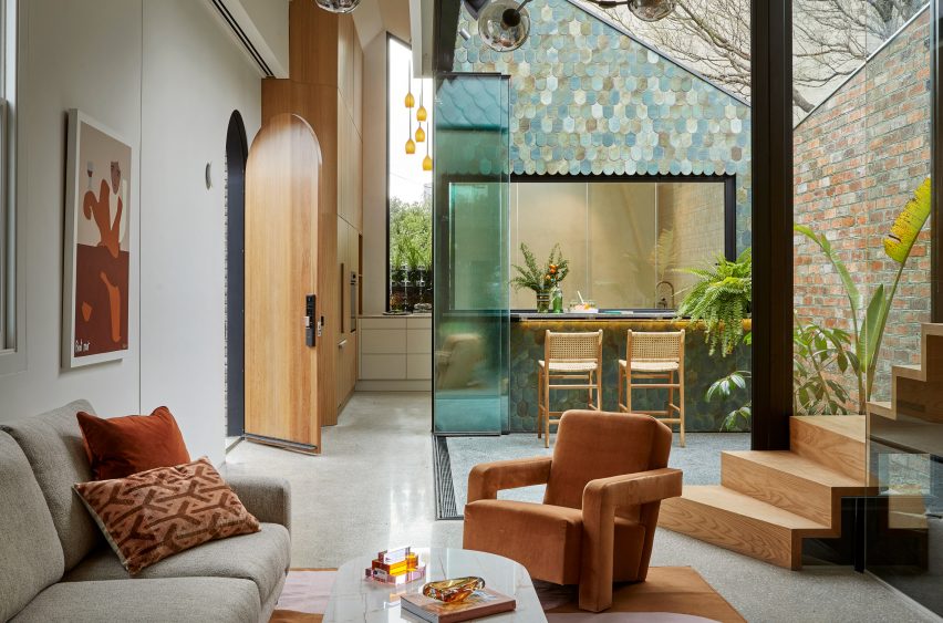 Гостиная с оранжевыми стульями и стеклянными стенами, опоясывающими двор с синей и зеленой плиткой