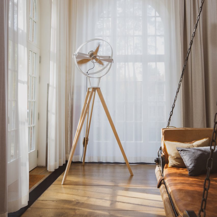 Aura wooden pedestal fan in the corner of a room with large windows