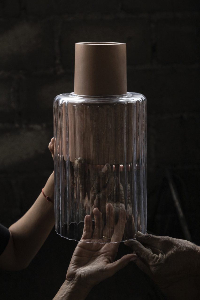 Photograph of two hands holding the red clay Barro lamp with a wavy transparent glass 