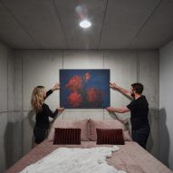 Photograph showing concrete bedroom with two people hanging art above bed