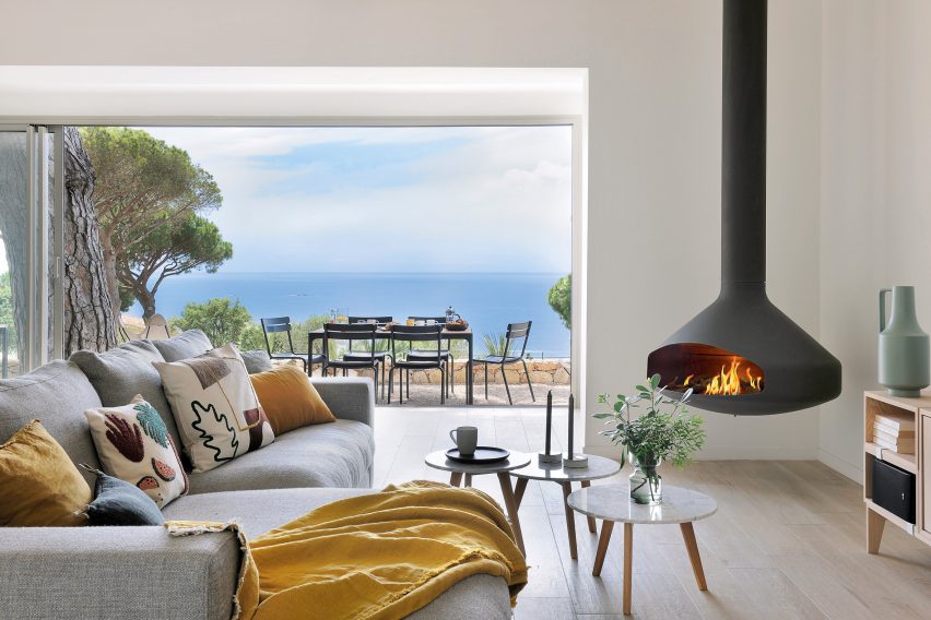 Focus fireplace in the corner of a white living room with a grey sofa and opening to terrace area