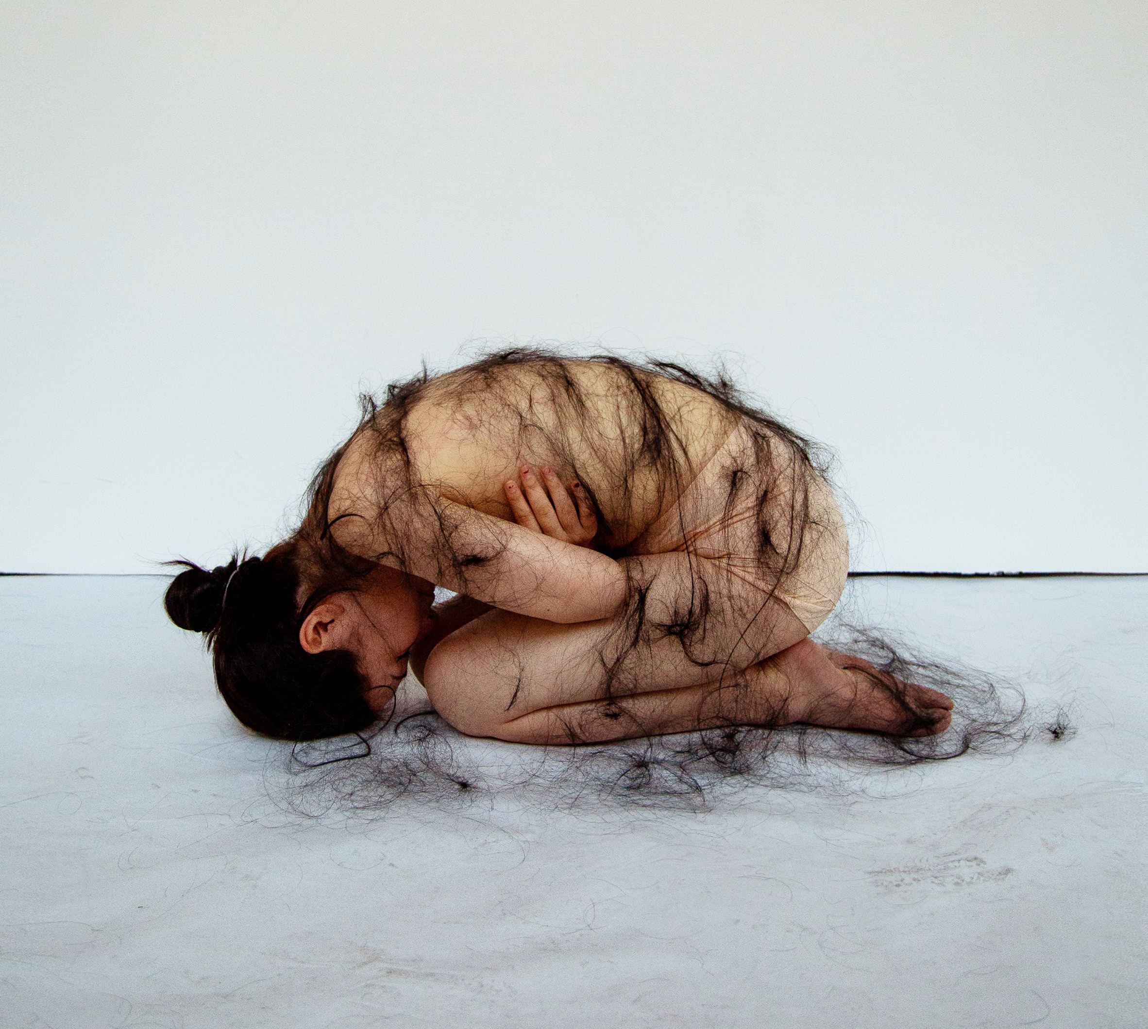 Person in foetal position with threads of hair draped on their back