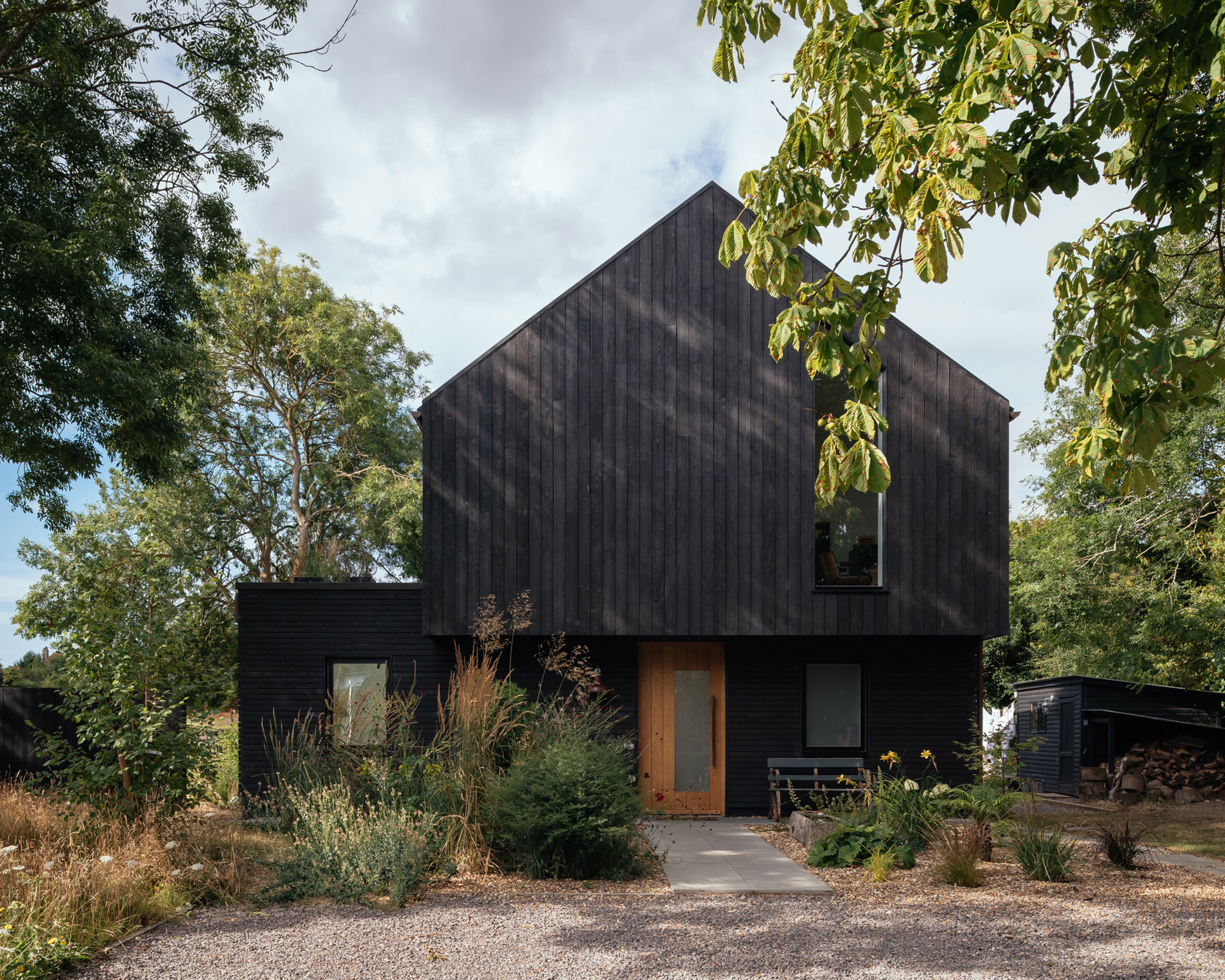 Black two-storey timber house with brown door by HAPA Architects