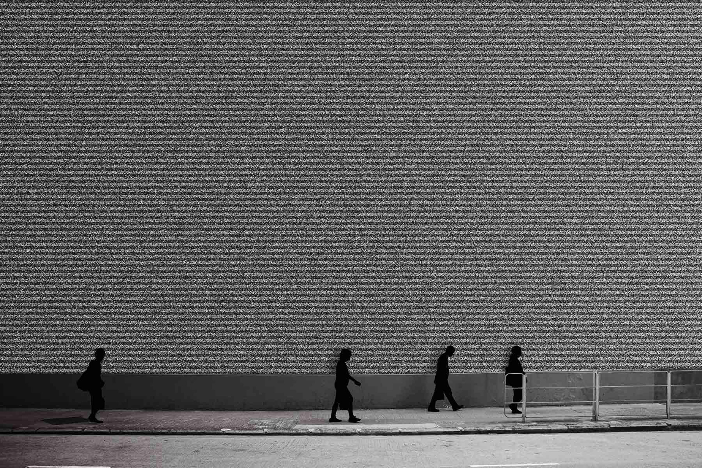 Photograph showing figures walking past a tall wall