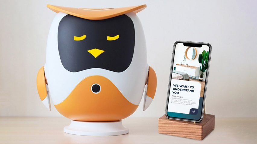 Robotic owl in black white and orange on a tabletop next to a phone