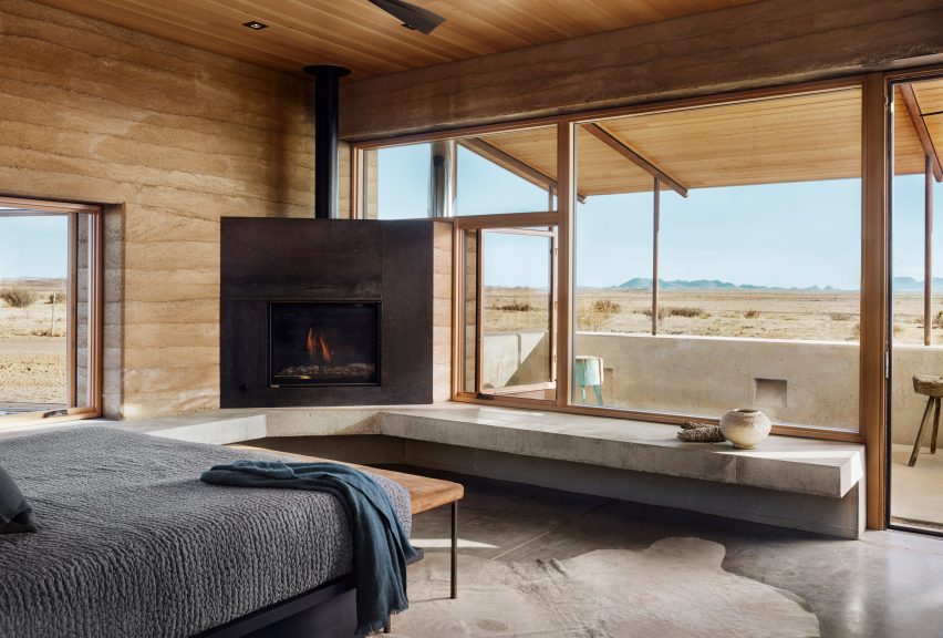 Bedroom with exposed rammed earth walls and porch with views of desert