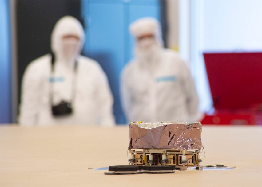 NeXolve technicians look on at a solar sail packaged up into a small shiny cube in the foreground