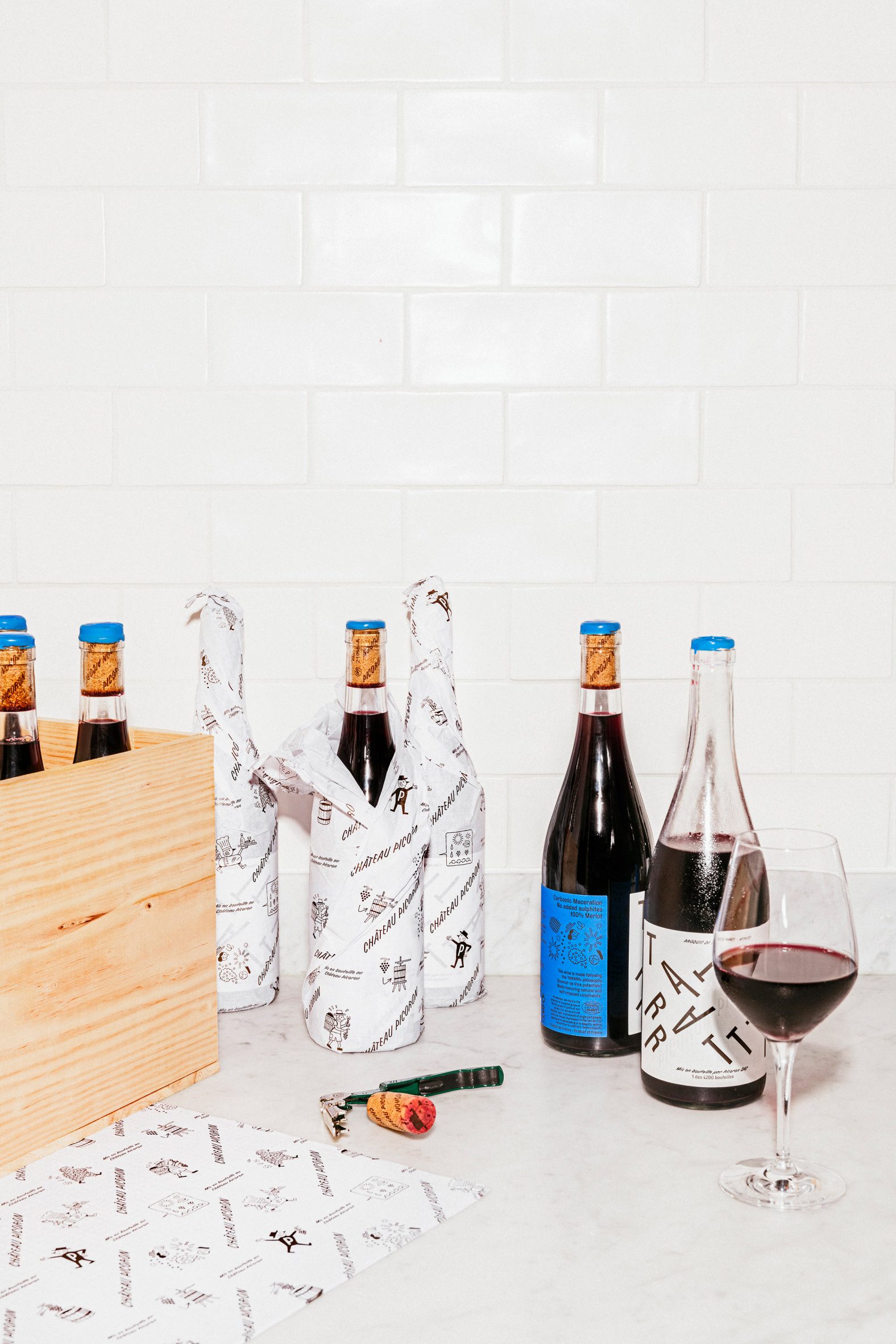 Photo of several bottles of red wine on a table, with some wrapped in branded paper and some in a crate