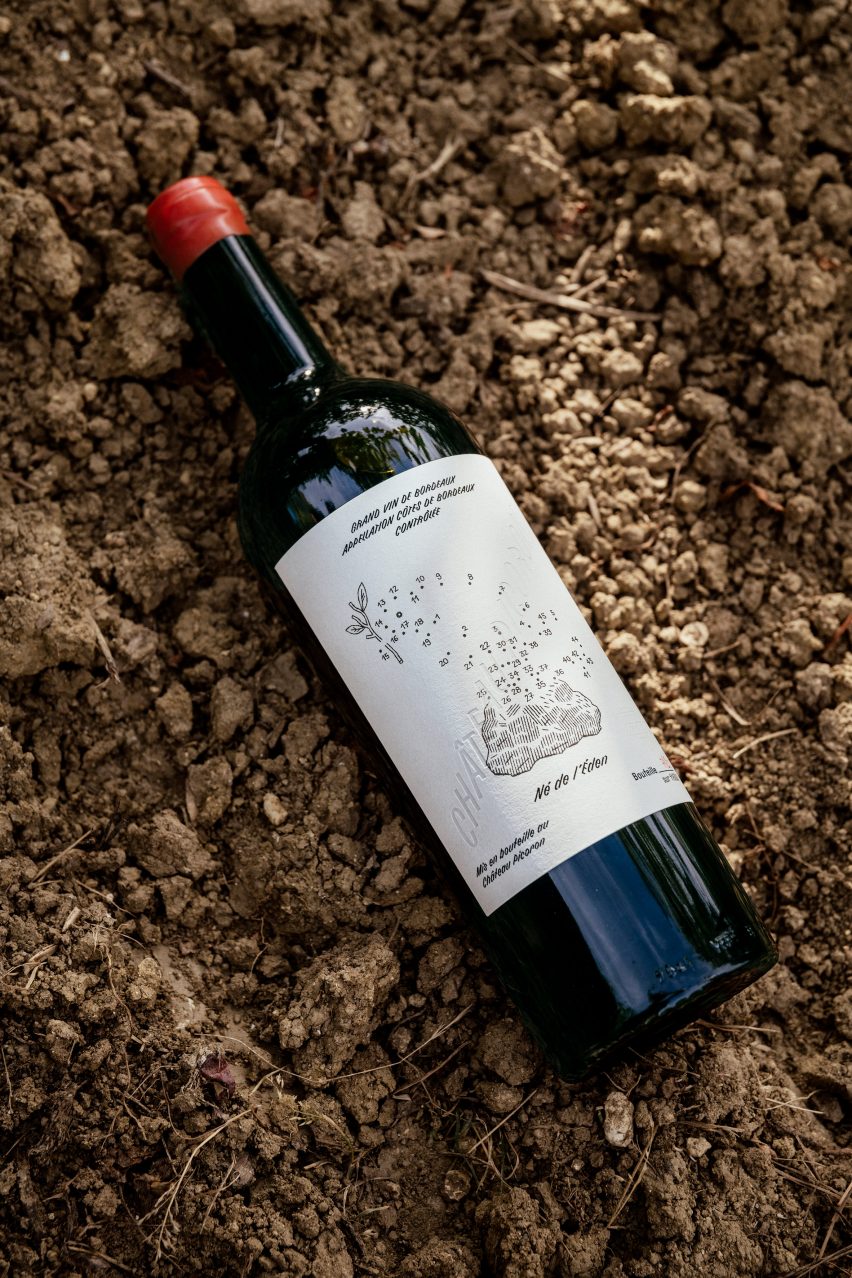 Photo of bottle of red wine with a dot-to-dot bird illustration on the label lying flat on the dirt ground