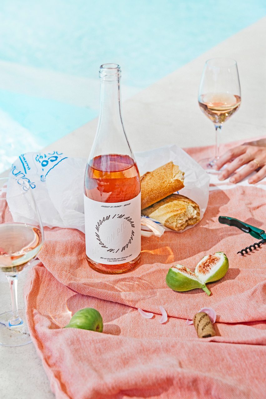 Bottle of rose open on a pink tablecloth surrounded by half-drunk wine glasses, torn baguettes and figs