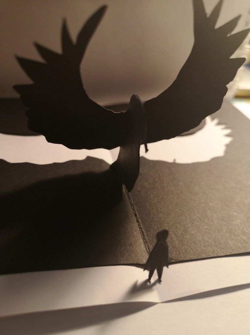 A black pop-up book of a small person and a large winged figure