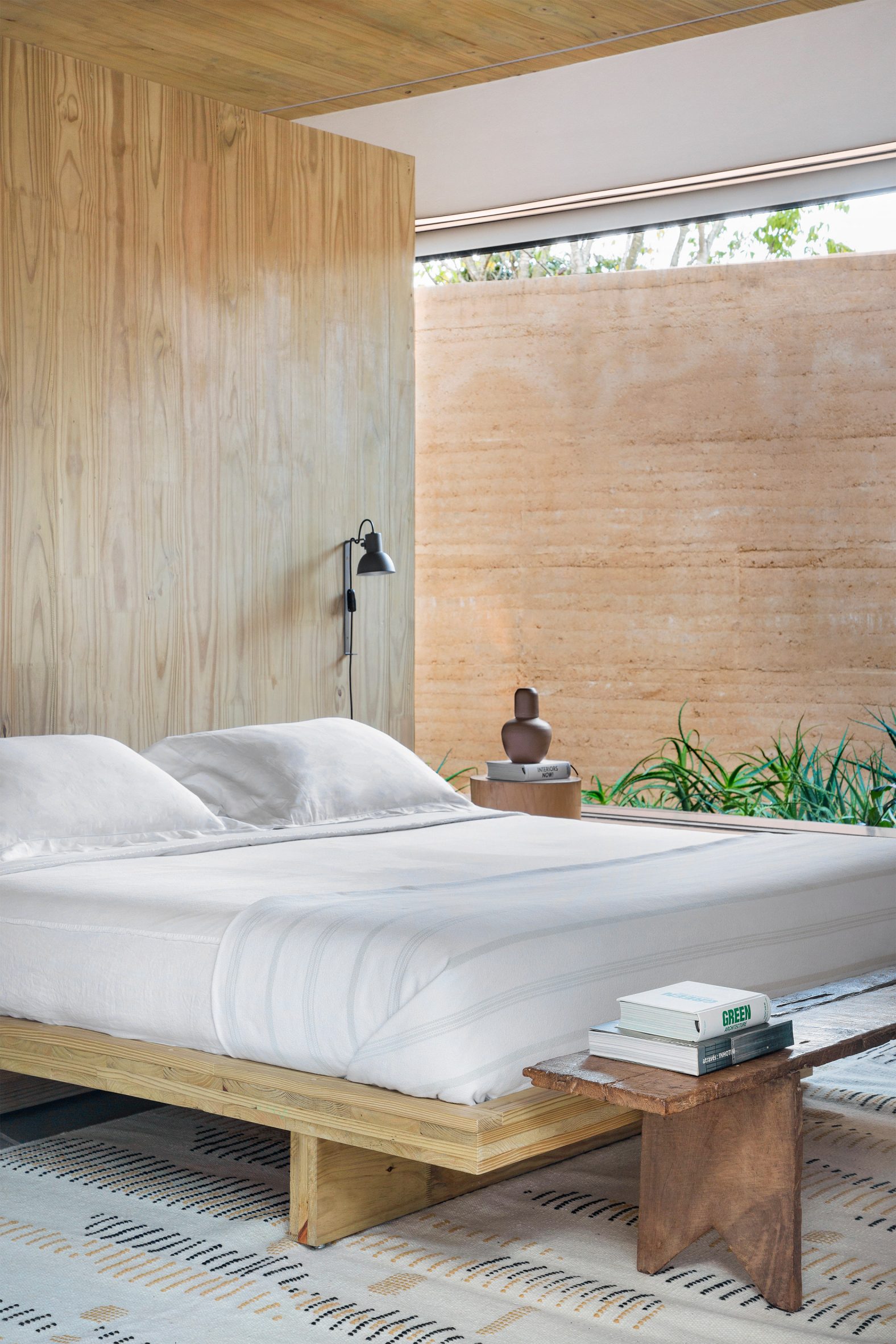 Bedroom with timber wall and floor-to-ceiling window showing rammed earth wall