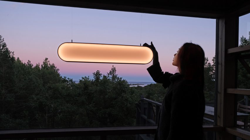 Woman turning on Sunne solar lamp by Marjan van Aubel in front of a window