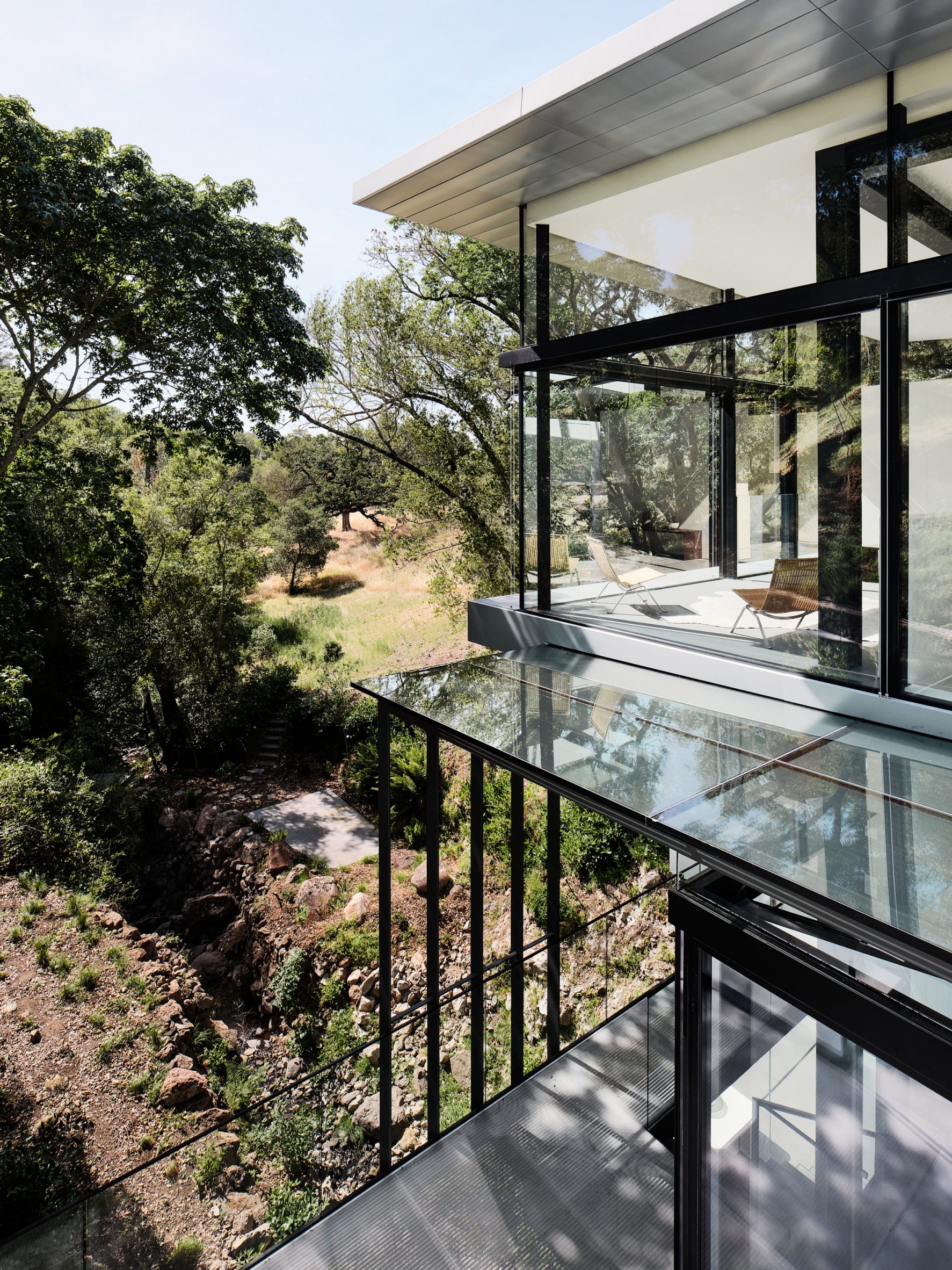 Upper storey of Californian creek house with glass panels, black columns, and zinc cladding
