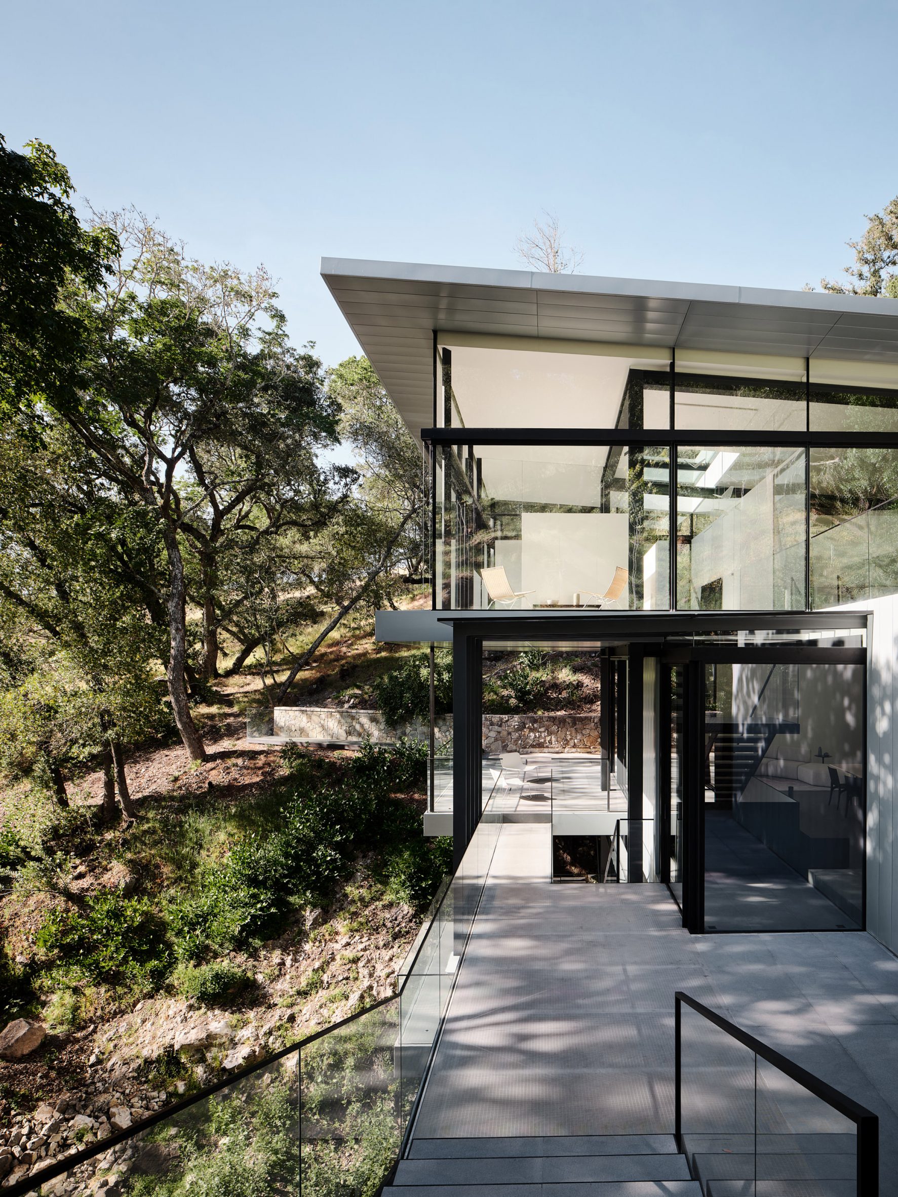 Suspension House by Fougeron Architecture in forested creek with sloped roof and glass walls
