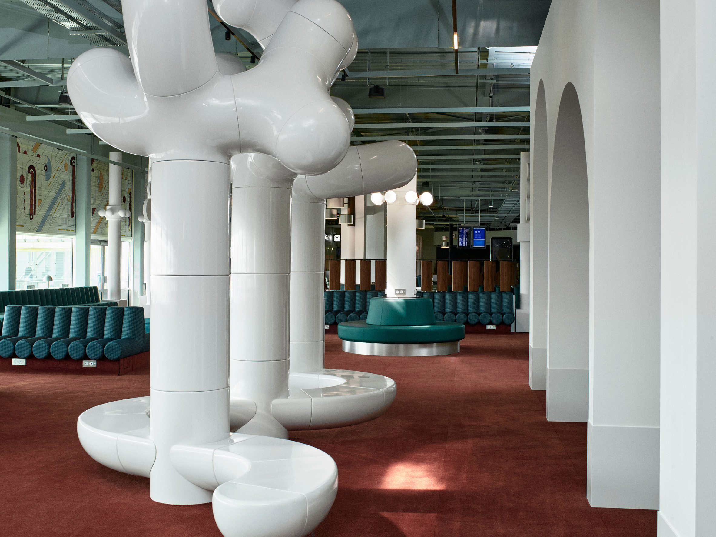 Photograph showing airport departure lounge with green bench seats and large tree-like rounded white sculptures