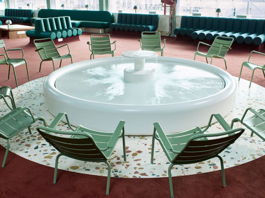 Photo showing the airport departure lounge with green chairs, white fountain and terrazzo floors