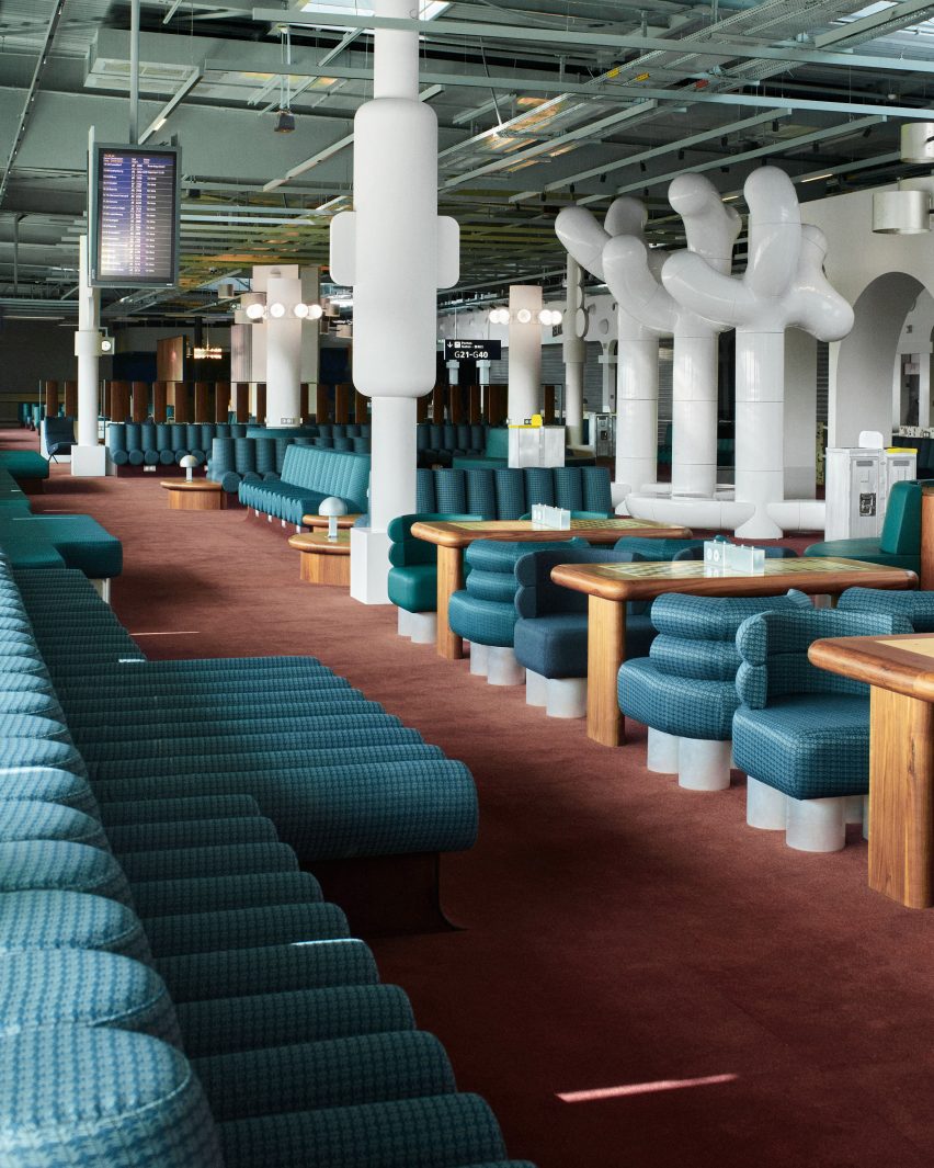 Фотография зала вылета в аэропорту с зелеными креслами и деревянными шахматными столами.