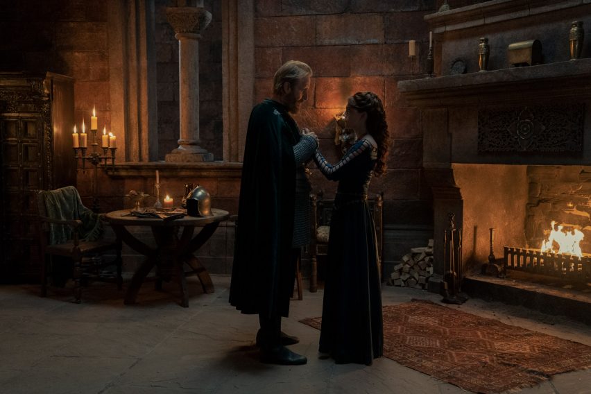 Two people in a castle room with an open fire