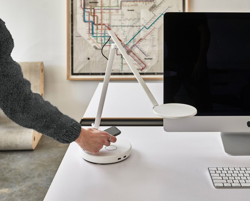 A hand putting a phone on a Nova desk lamp