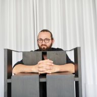 Photograph of black chair in front of white curtain with designer