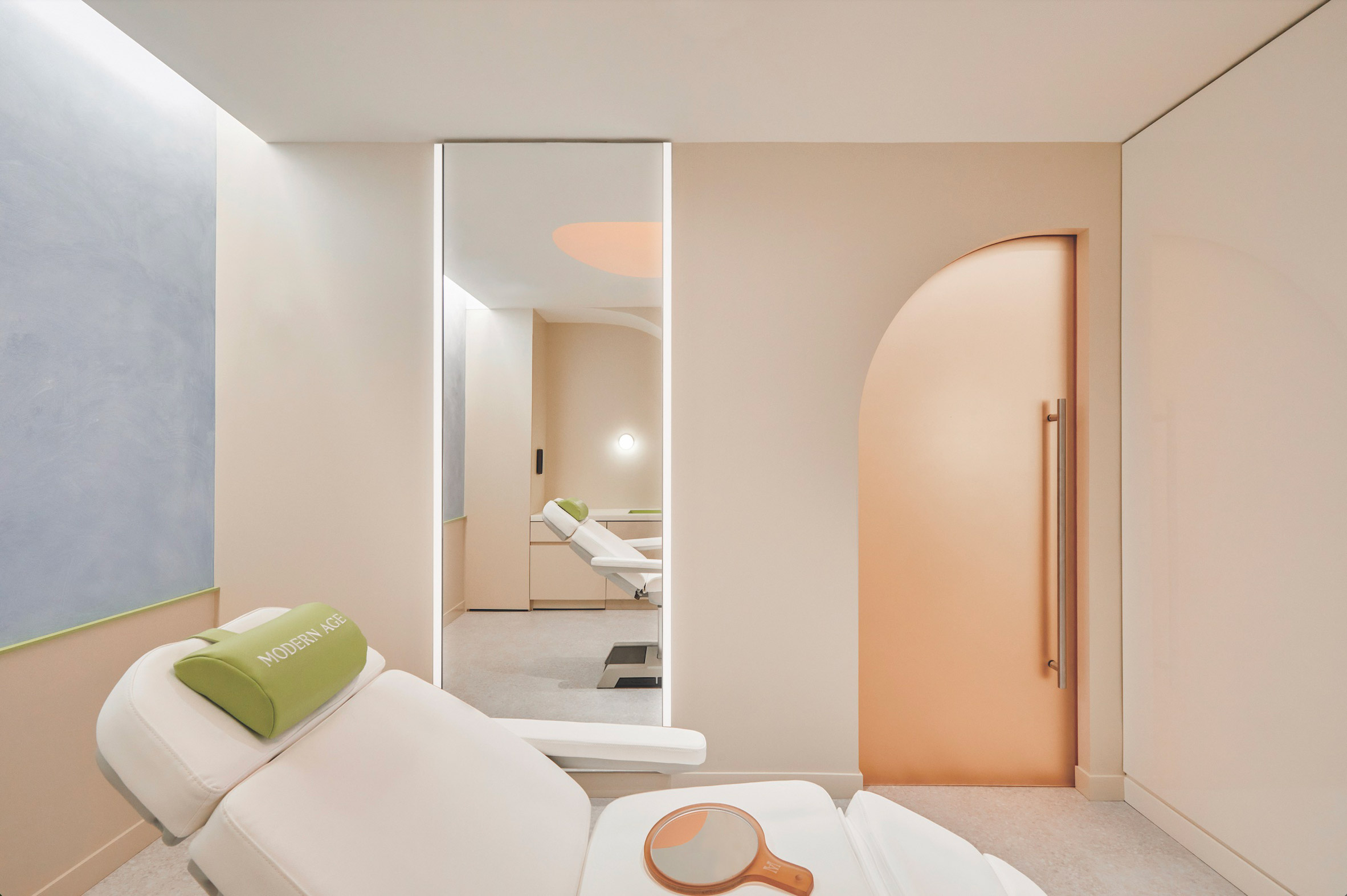 Suite at the Modern Age studio with a treatment bed in the foreground and peachy coral resin door in the background