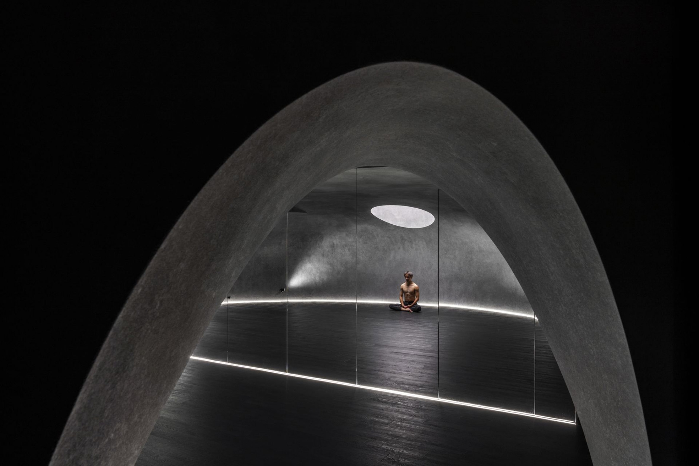 Person doing yoga in dark studio space beneath round skylight