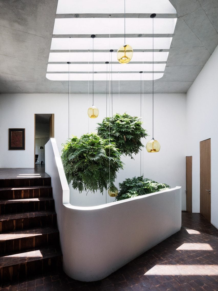White concrete spiral staircase with pendant lights and plants suspended from the ceiling