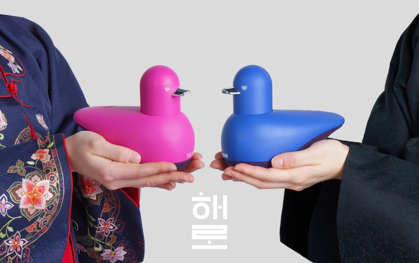 Photograph of two people holding blue and pink duck-like objects