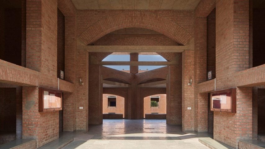 Looking through airy courtyard corridor of brick building with openings and windows and blue sky beyond