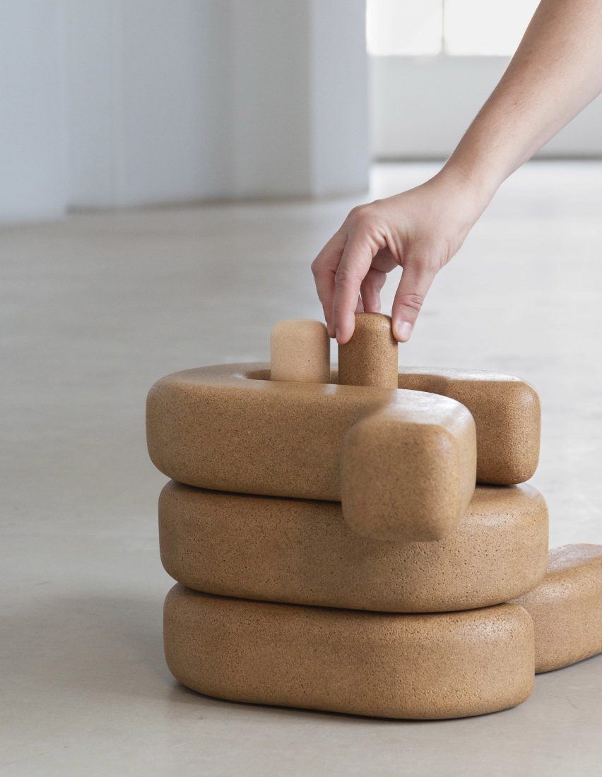 A hand assembles several pieces of brown, cork-like furniture by Eneris Collective