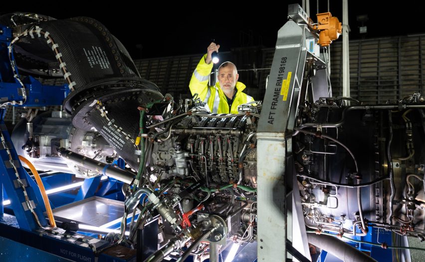 Photo of a man in hi-vis shining a light into the parts of a large aircraft engine