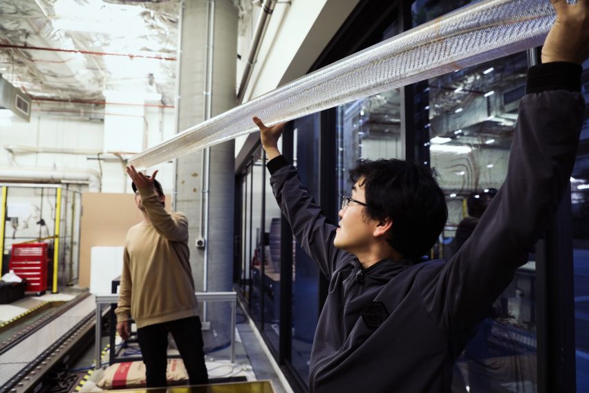 Photo of two people holding up a length of clear plastic tubing as if to install it on a ceiling