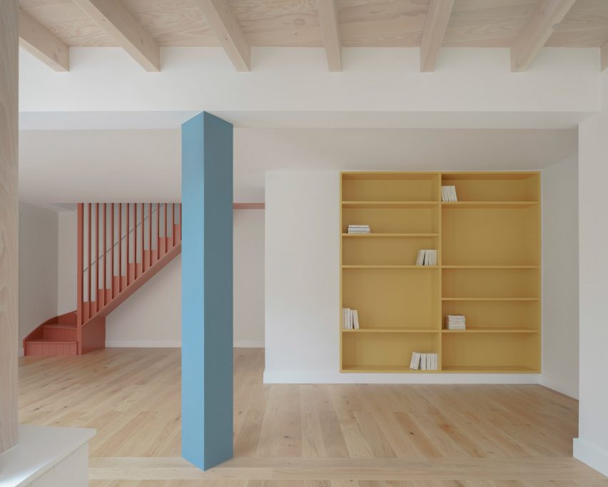 Pink staircase in room with blue pillar and yellow bookshelf