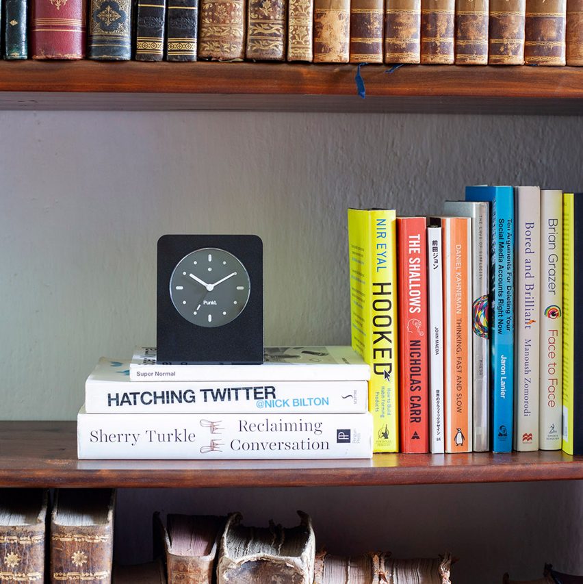 Black minimalist punkt clock with white hands sitting on bookcase