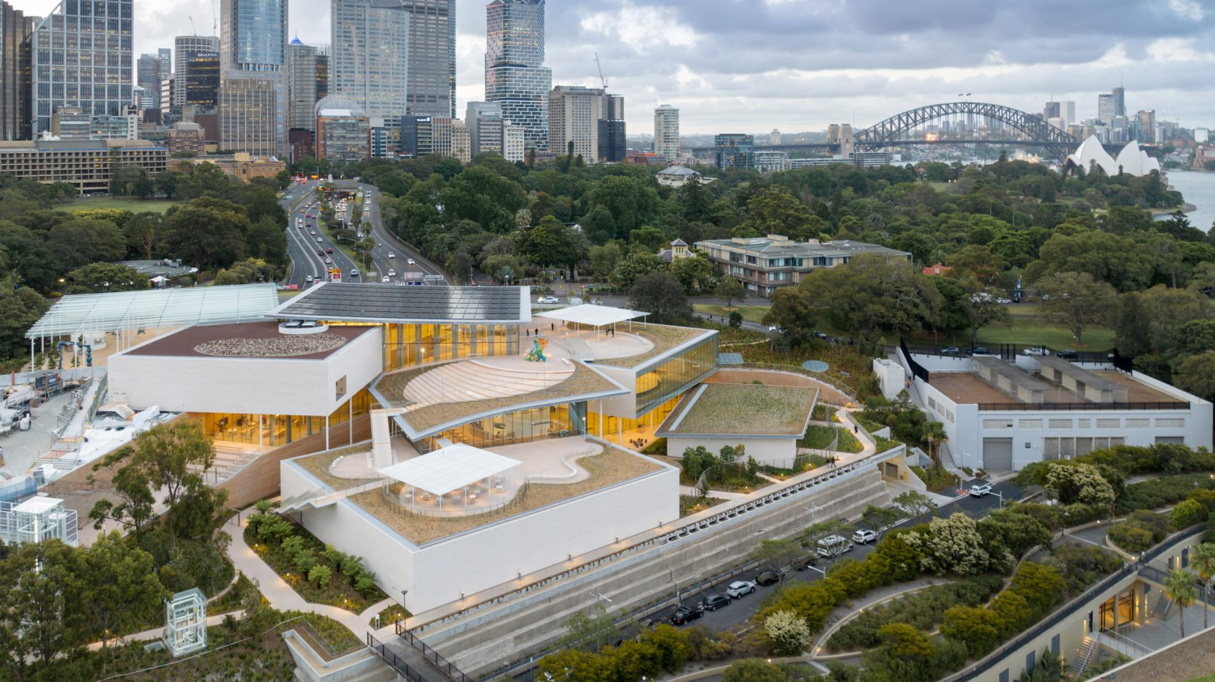 Aerial view of Sydney Modern art gallery showing the many pavilions on the slope over Sydney Harbour with the city and Opera House behind