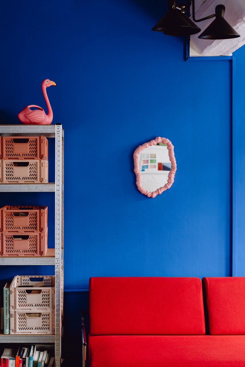 Picture of an office's interior with electric blue walls, a red couch and a small pink mirror