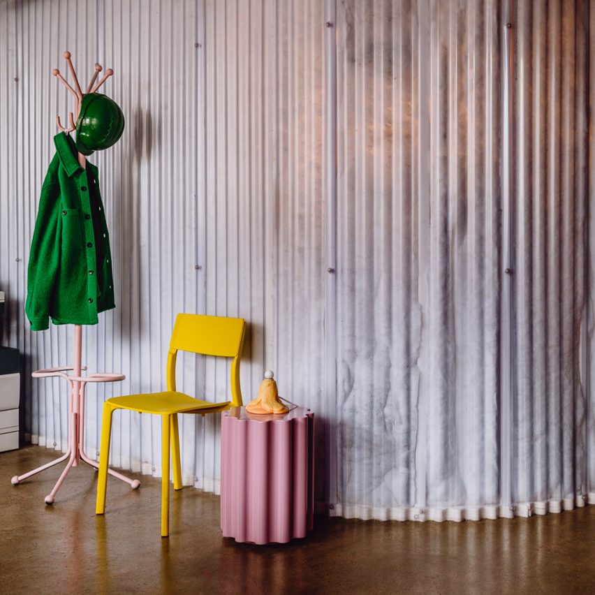 Изображение желтого стула и розового волнистого тумбочки перед стеной из переработанных пластиковых бутылок