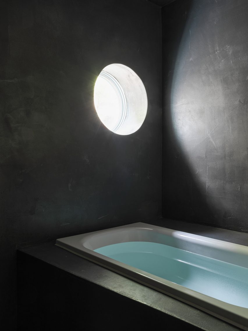 Black bathroom with bathtub lit by circular window