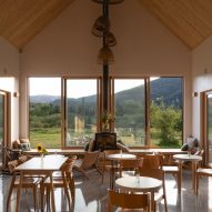 Cafe interior with wooden furniture and large windows overlooking a grassy hill