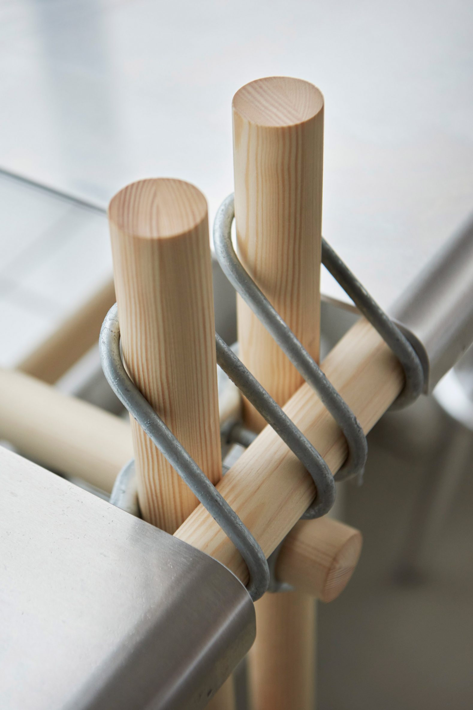 Close-up photo of looped metal joining elements holding cylindrical wooden parts together to make a seating frame