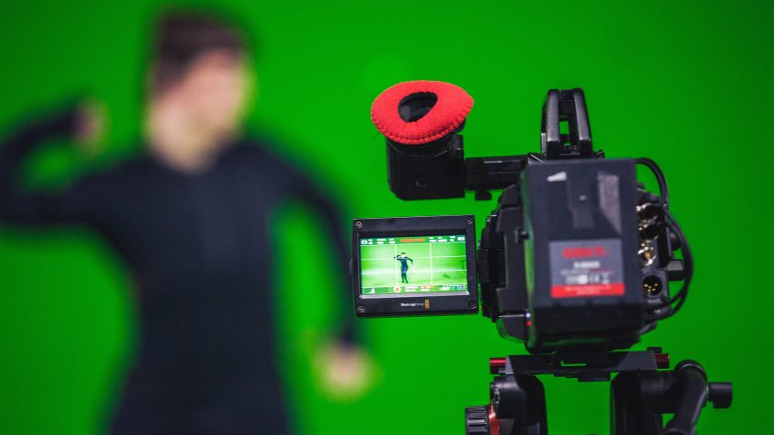 Photo of a camera filming an actor wearing a motion capture suit against a green screen