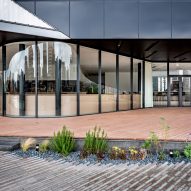 Paved entrance courtyard to a cultural building with curved glass walls