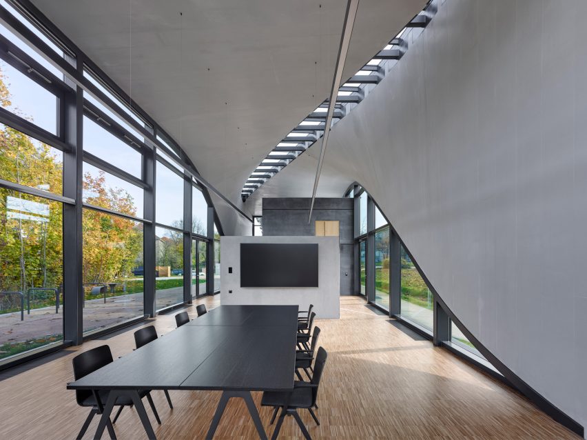 Photo of the Interior of the Cube building showing smooth concrete walls, undulating windows on all sides and a meeting table with a display screen on a partition