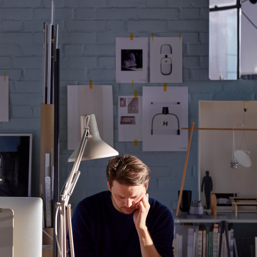 Daniel Rybakken sits at a desk in his studio, with drawings pinned to the wall behind him